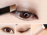 A close-up of a person's eye being applied with ExZachly Perfect's Two-tone eye shadow stick lazy eye shadow in shimmery bronze using a brush. The image also includes three smaller panels: one with the eye open showing the waterproof eyeshadow, one with the eye closed displaying it, and one of the two-color cosmetics being swatched on neutral skin types.