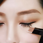 Close-up of a person's closed eye showing an ExZachly Perfect Two-tone eye shadow stick lazy eye shadow applying metallic eyeshadow to the lower eyelid. The person has well-defined eyebrows and winged eyeliner, enhancing the look with waterproof makeup for long-lasting wear.