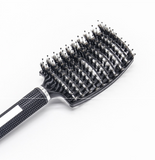 A black **ExZachly Perfect Hairbrush Anti Klit Brushy Haarborstel** with densely packed bristles is positioned against a white background. The brush features a textured handle with a glossy finish and a white rectangular marking. Ideal for scalp massage and detangling, the bristles appear to be a mix of plastic and boar hair.