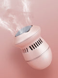 A compact, pink ExZachly Perfect Multifunctional Electric Foot File Grinder Machine Dead Skin Callus Remover emits a misty vapor while charging via USB. The device has a cylindrical body, slotted vents, and a rounded base. It is photographed against a matching pink background, slightly tilted upward as it releases the mist into the air.